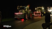 Mit Weihnachtslichtern geschmückte Tracktoren fahren eine Straße entlang. © NDR 