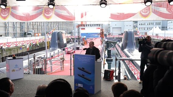 Bundeskanzler Olaf Scholz (SPD) steht an einem Rednerpult. Im Hintergrund ist das U-Boot zu sehen. Im Vordergrund weitere Presse. © dpa-Bildfunk Foto: Marcus Brandt