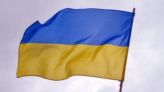 Eine ukrainische Flagge weht im Wind vor grauem Himmel. © IMAGO / ZUMA Wire 
