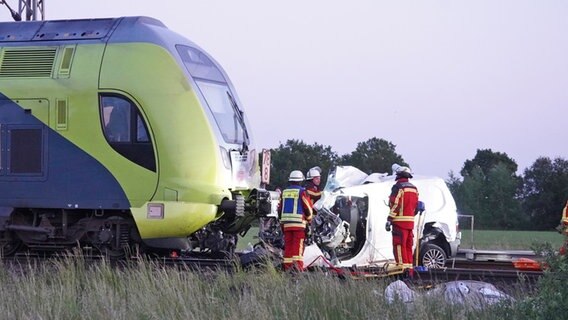 Einsatzkräfte der Feuerwehr stehen um einen weißen Lieferwagen mit Totalschaden, der mit einer Regionalbahn zusammengeprallt ist. © Daniel Friederichs 