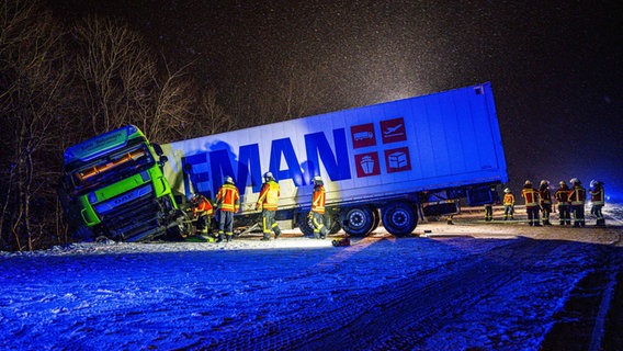 Feuerwehrleute stehen im Dunkeln neben einem in den Graben gerutschten Lkw. © nordpresse mediendienst/Sebastian Iwersen Foto: Sebastian Iwersen