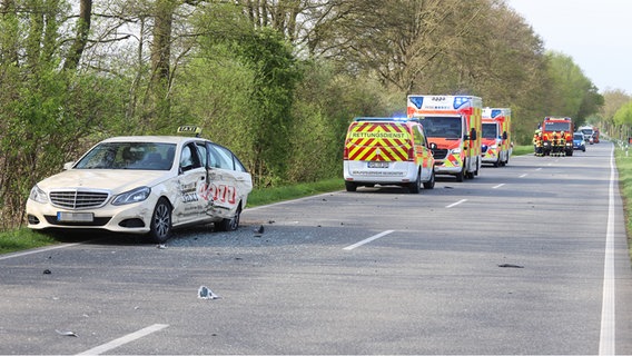 Ein Taxi steht am Rand einer Landstraße und wurde auf der linken Seite angefahren. Im Hintergrund befinden sich Rettungskräfte. © NDR Foto: Florian Sprenger