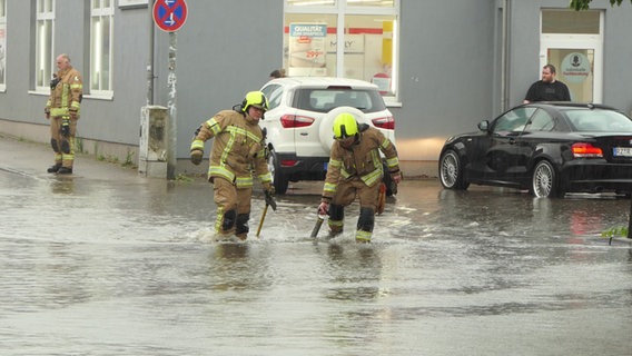 Während eines Unwetters laufen Feuerwehrleute in Mölln durch knietiefes Wasser über die Straße. © Daniel Friederichs Foto: Daniel Friederichs