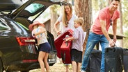 Eine Familie packt Gepäck in den Kofferraum eines Autos. © imago images / Zoonar II 