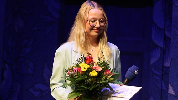 Ü18 Siegerin Ronja Sievertsen steht mit einem Blumenstrauß und einer Urkunde auf der Bühne im Ohnsorg Theater in Hamburg beim "Vertell doch mal". © NDR Foto: Oke Jens
