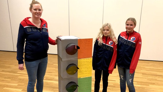 Jana Glindmeyer and two athletes from Vfl Pinneberg stand next to a traffic light.  © NDR Photo: Finn Ole Martins