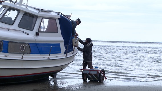 Ein Mann nimmt Lebensmittel von einem Boot an. Ein Mann nimmt Lebensmittel von einem Boot an. © NDR
