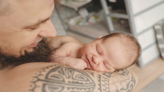 Ein Mann hält ein lächelndes Baby auf dem Arm. © picture alliance / Westend61 | Irina Heß 