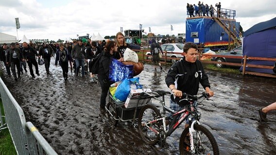 Festivalbesucher lassen ihr Gepäck von einem Jungen mit Fahrrad und Anhänger transportieren. © NDR Foto: Jörn Schaar