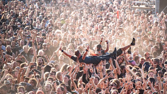 Festivalbesucher werden beim Wacken Open Air Festival beim Crowdsurfen über die Menge getragen. Das WOA gilt als größtes Heavy-Metal-Festival der Welt. © dpa/picture-alliance Foto: Daniel Reinhardt