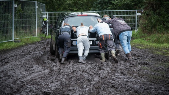 Eine Polizistin hilft einigen Festival-Besuchern in Wacken ein Fahrzeug aus dem Schlamm zu schieben. © Polizei Itzehoe 