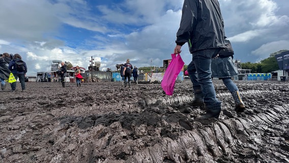 Auf dem Gelände des Wacken Open Air ist der Boden durch Regen aufgeweicht und nur noch Matsch und Schlamm. Einige Personen laufen mit Gummistiefeln durch den Schlamm. © NDR Foto: Tobias Gellert