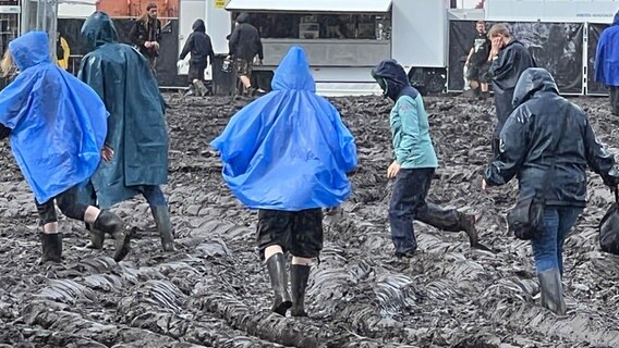 Auf dem Gelände des Wacken Open Air laufen Menschen in Gummistiefeln durch den Matsch. © NDR Foto: Tobias Gellert