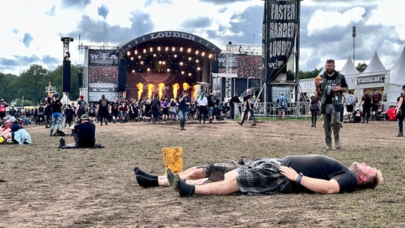 Eine Person liegt vor einer Bühne des Wacken Open Air 2023 rücklings vor einer Bühne. © NDR Foto: Jörn Zahlmann