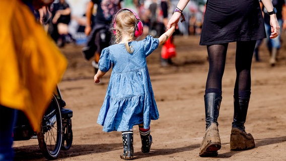 Wacken: Ein kleines Mädchen mit Gehörschutz läuft beim Wacken Open Air an der Hand der Mutter über das Festivalgelände. © dpa Bildfunk Foto: Axel Heimken