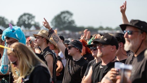Metalheads jubeln mit einer typischen Geste einer Band zu. © NDR Foto: Dominik Dührsen