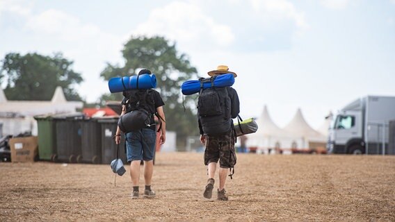 Zwei Festivalbesucher gehen mit ihrem Reisegepäck über das Wacken Open Air Festival. © dpa - Bildfunk Foto: Daniel Reinhardt