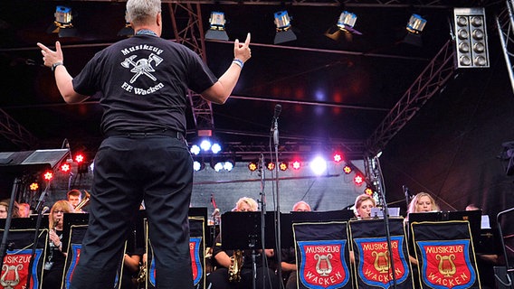 Ein Mann dirigiert das Orchester der freiwilligen Feuerwehr beim Wacken Open Air 2016. © dpa/bildfunk Foto: Carsten Rehder