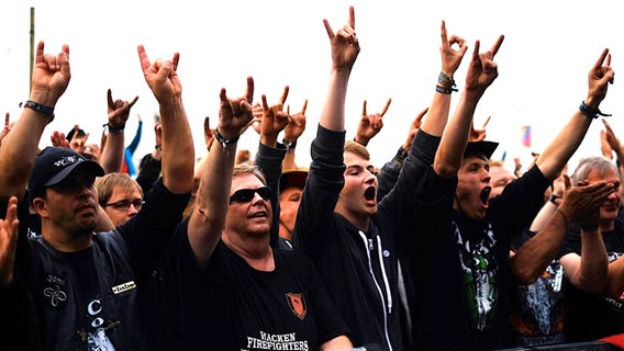 Heavy-Metal-Fans feiern 2016 das Orchester der freiwilligen Feuerwehr Wacken. © dpa/bildfunk Foto: Axel Heimken