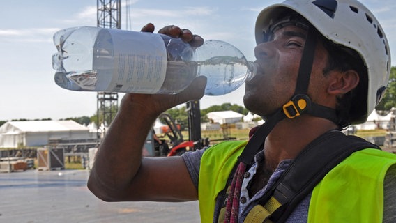 Ein Bauarbeiter trinkt Wasser aus einer Plastikflasche auf dem Festival-Gelände in Wacken. © NDR Foto: Eva Schulze-Gabrechten