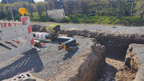 Ein Arbeiter schweißt an einem Nahwärmerohr neben einem ausgehobenen Schacht in Hürup. © NDR Foto: Peer-Axel Kroeske