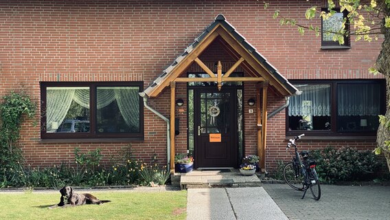 Ein Hund liegt im Vordergarten eines Hauses © NDR Foto: Torsten Creutzburg