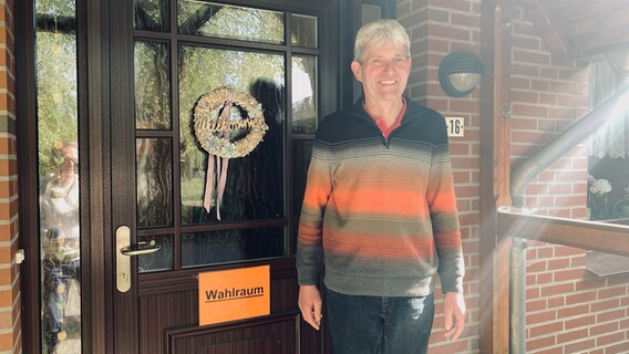 Bürgermeister Klaus Groenewold steht vor seiner Haustür mit der Aufschrift "Wahlraum" © NDR Foto: Torsten Creutzburg