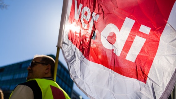 Ein Teilnehmer einer Kundgebung anlässlich eines Warnstreiks hält  eine Verdi-Fahne, durch die die Sonne hindurch scheint. © dpa | picture alliance | Christoph Soeder Foto: Christoph Soeder