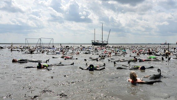 Menschen liegen verdreckt bei Ebbe im Watt, im Hintergrund ist ein Segelschiff zu sehen. © NDR Foto: Carsten Rauterberg