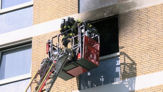 Ein Feuerwehrmann steht im Korb einer Drehleiter an einem ausgebrannten Fenster eines Hochhauses in Wedel. © TV- NEWS KONTOR 