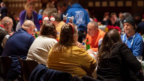 Menschen sitzen an einem langen Tisch beim Weihnachtsessen für Wohnungslose in der Stadtmission Kiel. © Stadtmission Kiel/Kim Hase Foto: Kim Hase