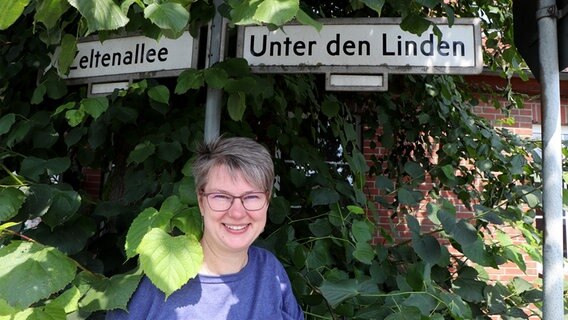 Petra Wede steht unter Straßenschildern mit den Titel "Unter den Linden" und "Zeltenallee" im Ort Berlin im Kreis Segeberg. © NDR Foto: Tobias Senff