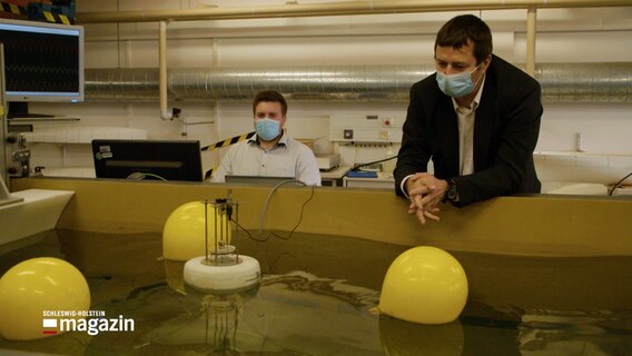 Forscher der FH Kiel beobachten in einem Wasserbecken ein künstliches Wellenkraftwerk.  