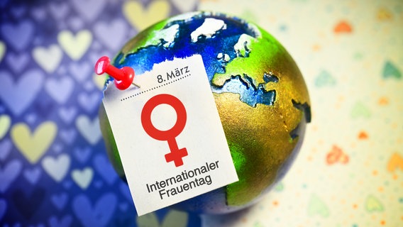 Auf einem Globus ist ein Kalenderblatt des 8. März mit einem Pin. Befestigt. Darauf steht das Symbol für Weiblich und der Schriftzug Internationaler Frauentag. © picture alliance / CHROMORANGE Foto: Christian Ohde