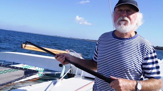 Der Weltumsegler Burghard Pieske hält ein Ruder seines Boots in den Händen. © NDR Foto: Julian Marxen