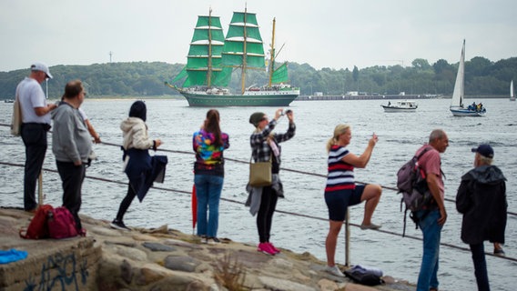 Menschen beobachten die "Alexander von Humboldt 2" während der traditionellen Windjammerparade zum Abschluss der Kieler Woche.  Foto:  Gregor Fischer/dpa