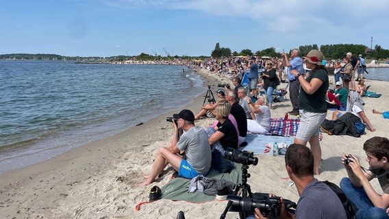 Zahlreiche Menschen tummeln sich an einem Strandabschnitt, um die Windjammerparade 2023 in Kiel zu beobachten. © NDR Foto: Paul Wessel