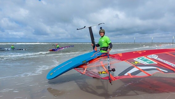 Windsurfer Meno Büchler geht am Strand von St. Peter-Ording mit seinem Windsurf ins wasser. © NDR Foto: Laura Albus