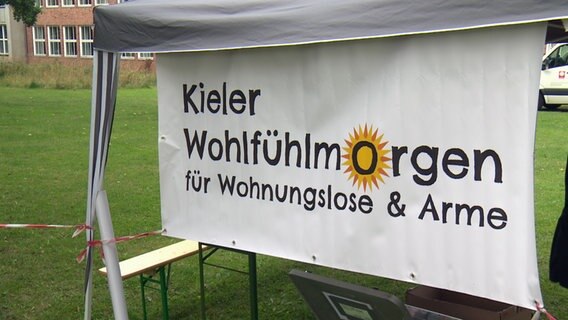 Ein weißer Banner mit der Aufschrift "Kieler Wohlfühlmorgen" hängt an einem Zelt. © NDR 