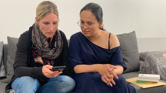 Zwei Frauen sitzen auf einer  Couch und blicken auf ein Handy. © NDR Foto: Corina Below