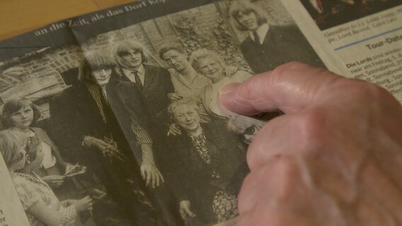 Eine ältere Frau zeigt auf ein Foto in einer Zeitung, das sie zusammen mit der deutschen Rockband The Lords zeigt.  