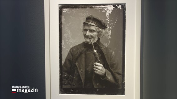 Ein gerahmtes schwarzweiß Foto zeigt einen alten Mann mit Pfeife.  