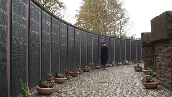 Ein älterer Herr liest eine Wand mit Namen von gefallenen Soldaten. © NDR 