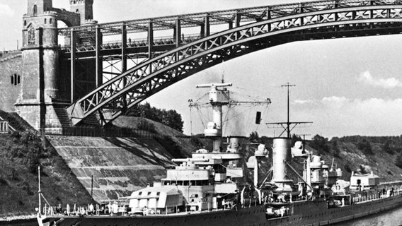 Auf einem schwarzweiß Foto fährt ein Kriegsschiff unter einer Brücke durch. Auf einem schwarzweiß Foto fährt ein Kriegsschiff unter einer Brücke durch. © NDR