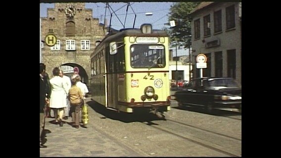 Die Flensburger Straßenbahn fährt durch eine Straße in der Nordstadt, im Hintergrund ist das Nordertor zu sehen © NDR 