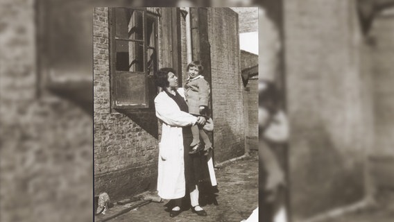 Eine vergilbte Schwarzweiß-Aufnahme zeigt eine Mutter mit ihrem Kind auf dem Arm. © Stadtarchiv Friedrichstadt 