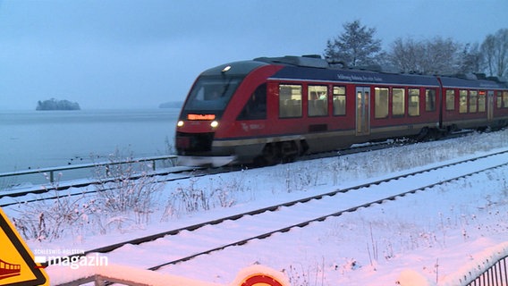 Ein Zug rast durch eine schneebedeckte Landschaft. © NDR 