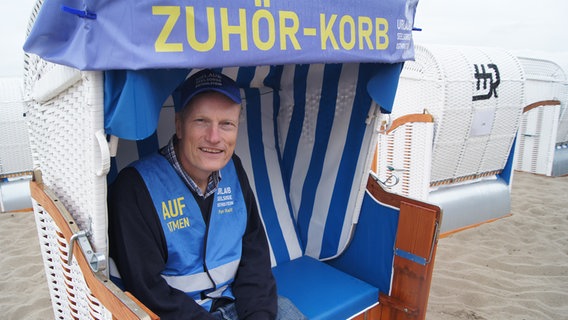 Ralf Winterberg sitzt in einem Strandkorb mit der Aufschrift "Zuhör-Korb" und lächelt für ein Foto in die Kamera © NDR Foto: Astrid Wulf