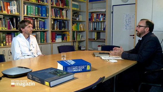 Prof Dr. Jan Rupp (l.)  sitzt mit Reporter Philip Schroeder an einem Tisch.  