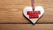 Ein Herz mit einem Aufkleber, auf dem "Mein Name" steht, hängt vor einer Holzwand. © photocase Foto: boing